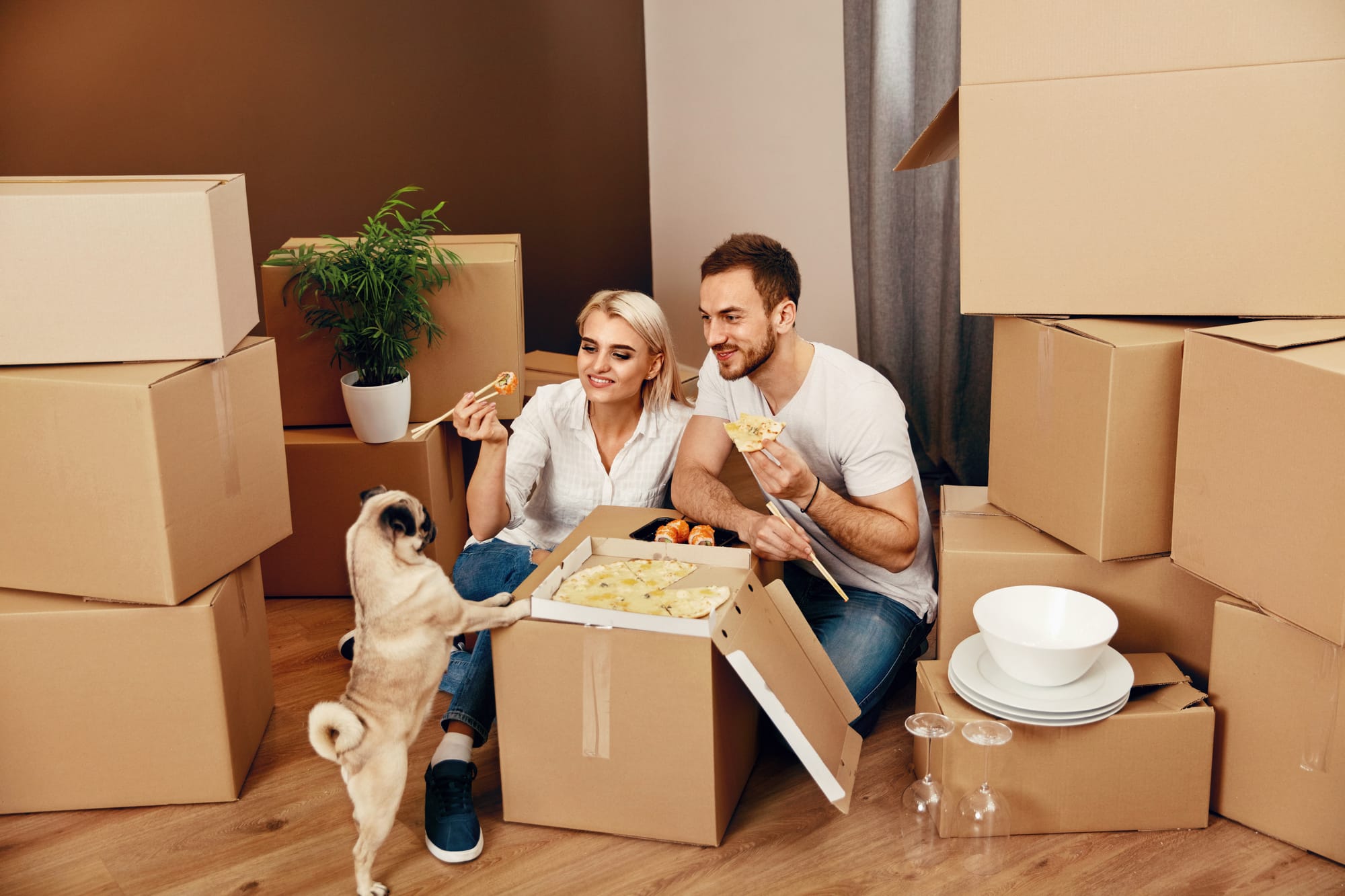 Man and woman eating with dog on moving box.